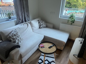 A modern living room with a sectional sofa, a small round table, and a view of a garden through a window. - Apartment in Dorfzentrum Near Lake (Feld am See)