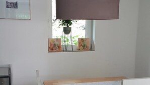 Une pièce avec une table en bois, une fenêtre ornée d’œuvres d’art et un radiateur.