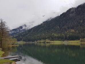 A calm lake surrounded by forested mountains, a dock, and a small building. - Apartment in Dorfzentrum Near Lake (Feld am See)