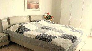 Un lit bien fait, recouvert d’une courtepointe à motifs, une table de chevet avec une lampe et un vase de fleurs posé sur la table de chevet.