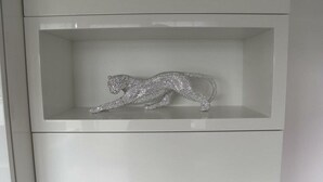 Un meuble blanc avec une étagère sur laquelle se trouve une sculpture représentant un léopard bondissant, en argent et ornée de strass.