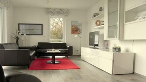 Un salon moderne avec un canapé gris, un tapis rouge et un meuble blanc doté de portes en verre.
