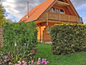 Een houten chalet met schuin dak, schoorsteen en balkon.