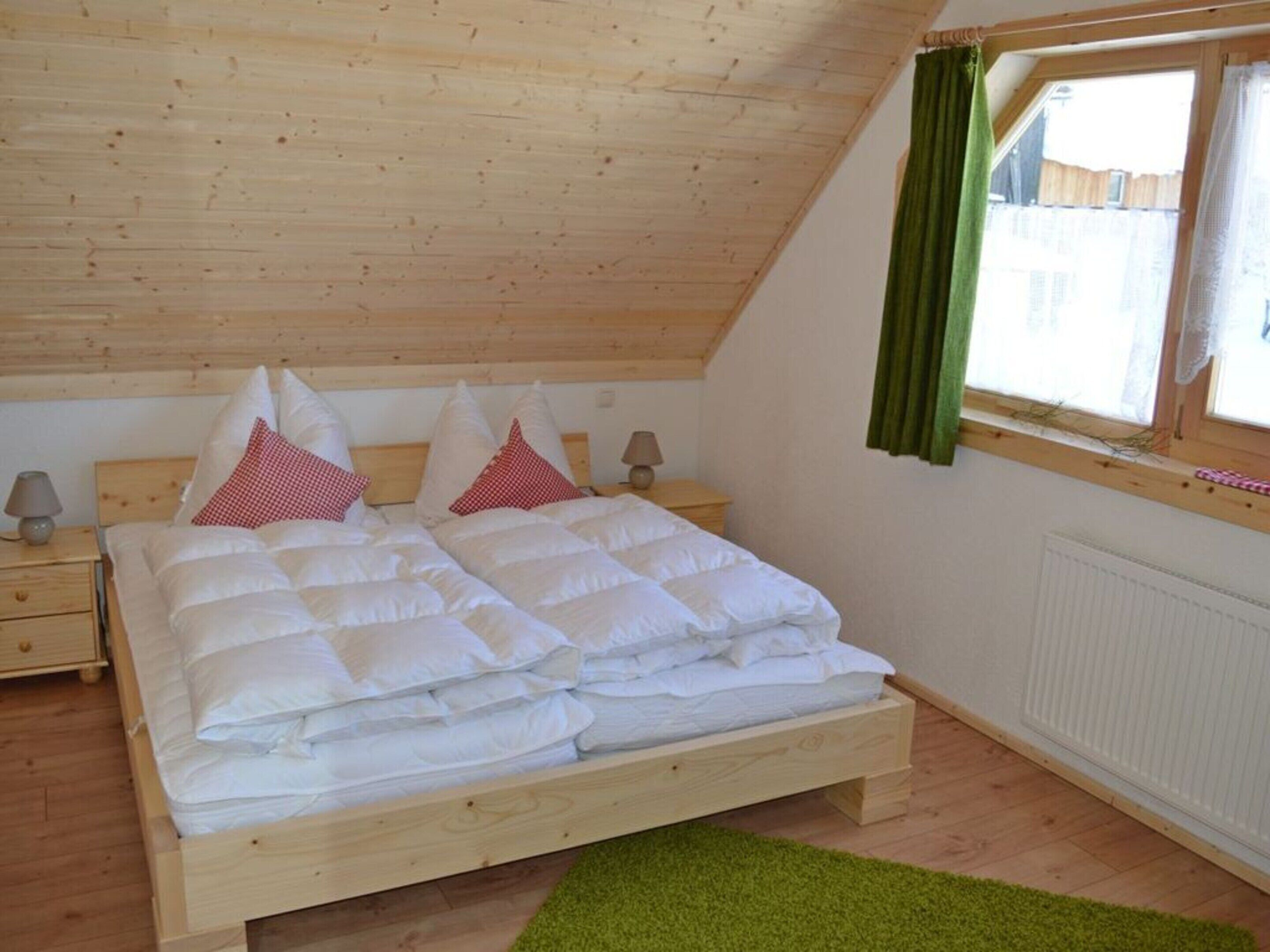 A bedroom with a wooden bed, a nightstand, a lamp, and a window with curtains.