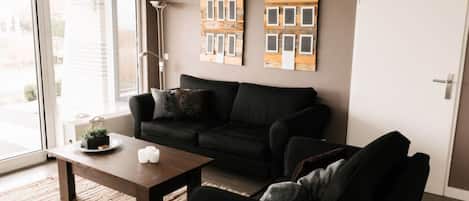 A living room with a black sofa, a wooden coffee table, and two wooden house-shaped decorations on the wall.