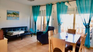 Ein Wohnzimmer mit einer Couch, Stühlen, einem Esstisch und türkisblauen Vorhängen.