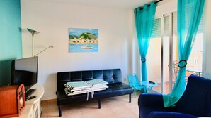 Ein Wohnzimmer mit einer schwarzen Couch, einem kleinen Tisch, einem Fernseher und einem Bild einer Küstenlandschaft.