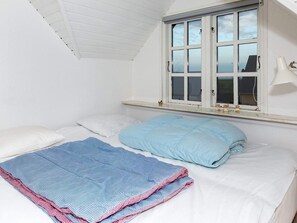 A bedroom with a single bed, white bedding, a blue quilt, a window with white shutters, and a small bedside lamp. - 6 Person Holiday Home in Logstor (Logstor)