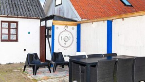 A courtyard with a table and chairs, a decorative wall, and a building with a red roof. - 6 Person Holiday Home in Logstor (Logstor)