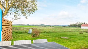 An outdoor seating area with a table and chairs, a wooden fence, and a view of a grassy field. - 6 Person Holiday Home in Logstor (Logstor)