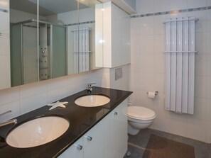 A modern bathroom with two sinks, a toilet, and a glass shower enclosure. - Stylish Stay w/ Sea Views (Middelkerke)