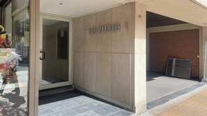 Entrada de um edifício com porta de vidro, placa indicando "MERMAID 1" e chão de azulejos.