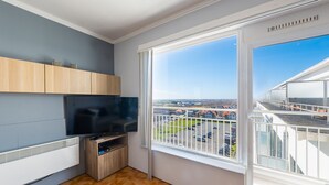 Eine moderne Wohnung mit großem Fenster, Flachbildfernseher, Holzausstattung und Fliesenboden.