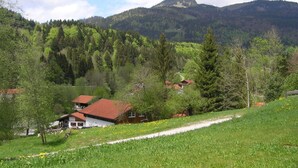 Paisaje rural con una casa en una colina, rodeada de vegetación y montañas.
