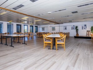 A spacious conference room with multiple tables and chairs, large windows, and artwork on the walls.