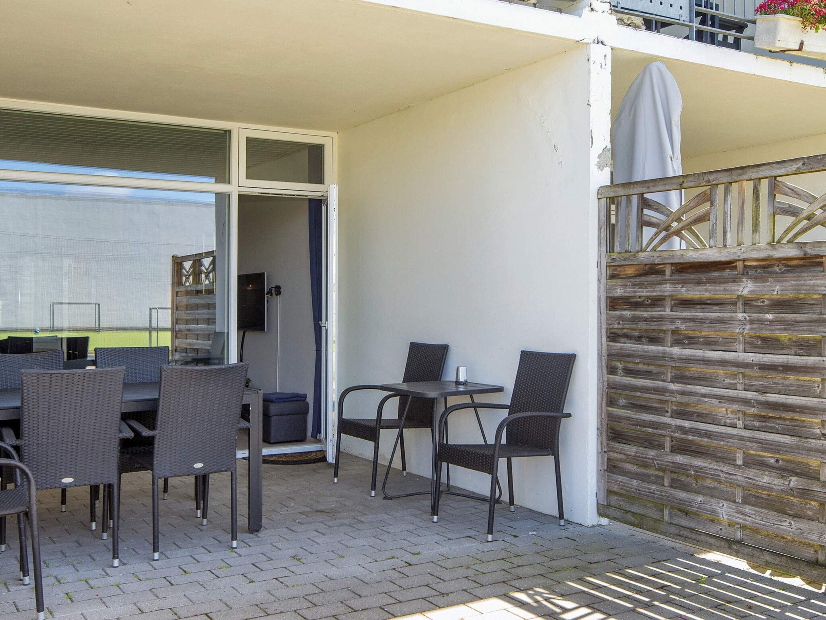 An outdoor patio with a table and chairs, a covered area, and a wooden fence.