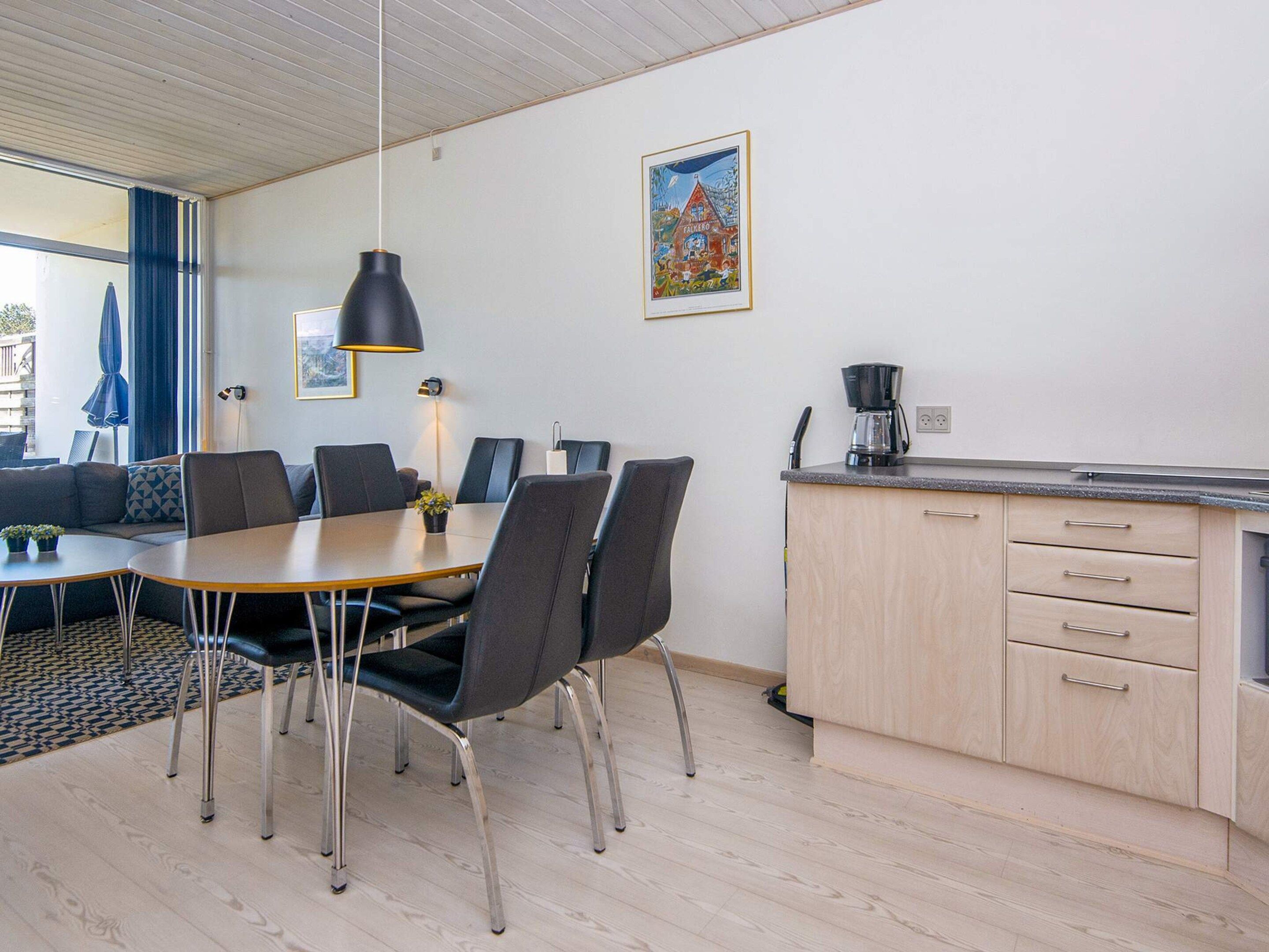 A modern kitchen with a dining area, wooden cabinets, and a coffee maker.