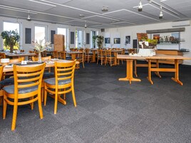 Ein geräumiger Essbereich mit Holztischen und -stühlen, großen Fenstern und Zimmerpflanzen.
