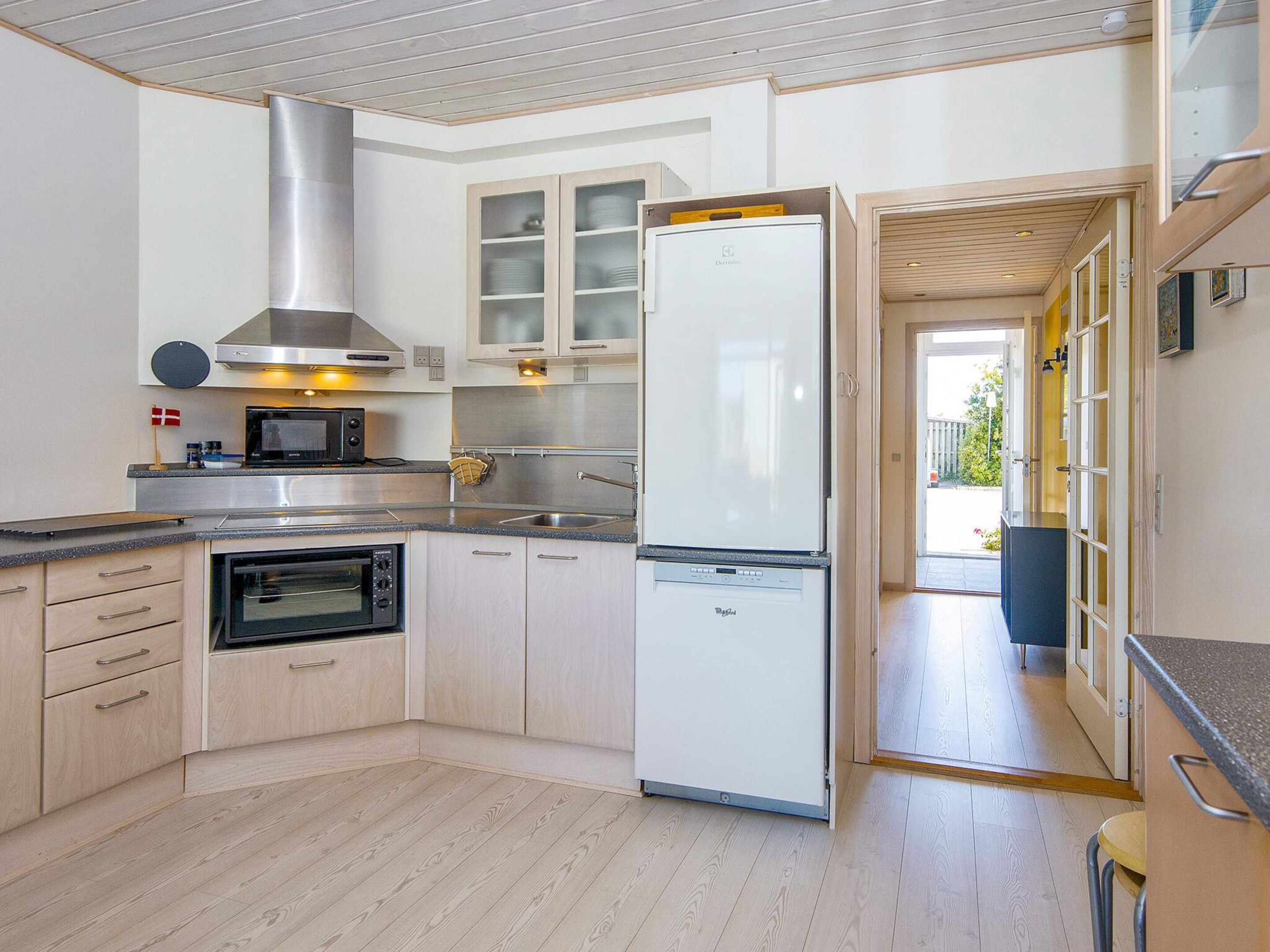 A modern kitchen with a built-in oven, microwave, and stainless steel range hood. There is a large refrigerator and wooden cabinets.