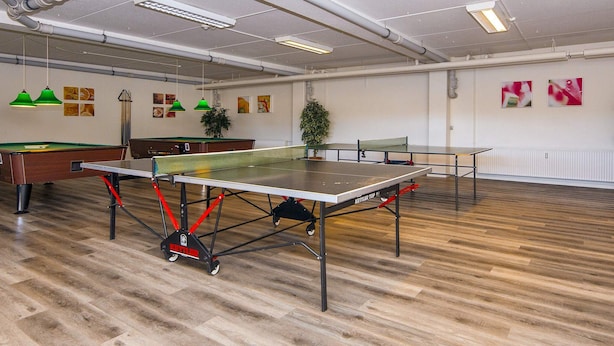 Una habitación amplia con dos mesas de ping pong, una mesa de billar y una mesa de futbolín.