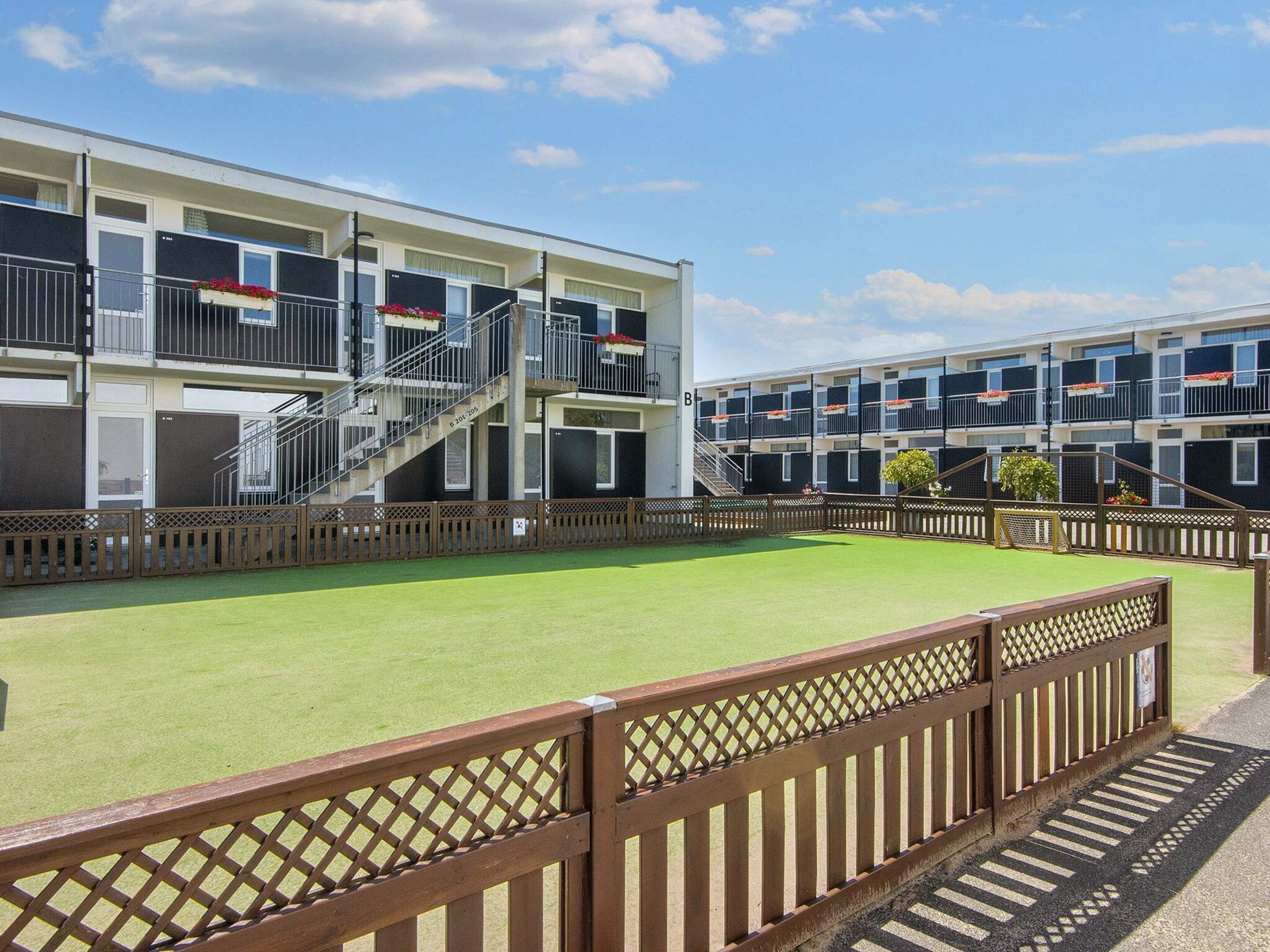 A multi-story hotel with balconies, a central staircase, and a green lawn area.