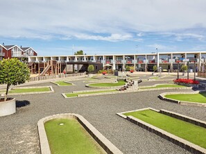 A courtyard with a children's play area, a small bridge, and a building with multiple balconies and outdoor seating. - 4 Person Holiday Park Home in Glesborg (Glesborg)