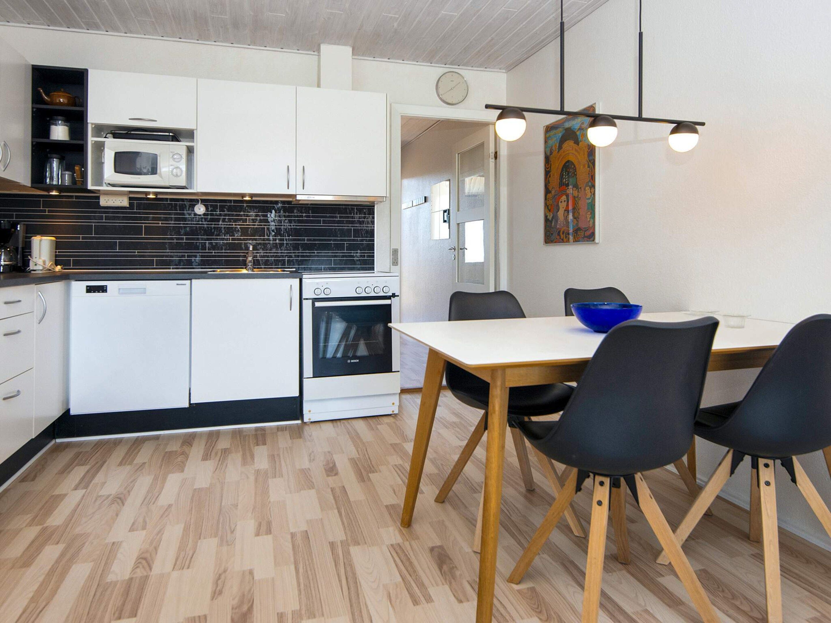 A modern kitchen with white cabinets, a microwave, an oven, and a dining area with a wooden table and black chairs.