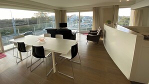 A modern living room with a dining area, large windows, and a view of the city. - Apartment in Nieuwpoort With Terrace (Nieuwpoort)