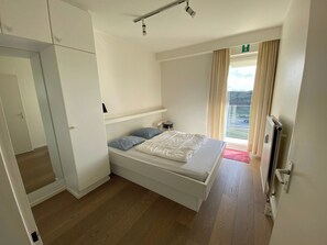Une chambre à coucher avec un lit, un radiateur, une fenêtre avec des rideaux et une porte.