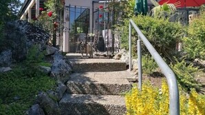A building with a stone staircase leading to a covered entrance, surrounded by greenery and a metal railing. - Donautal Comfortable Holiday Residence (Irndorf)