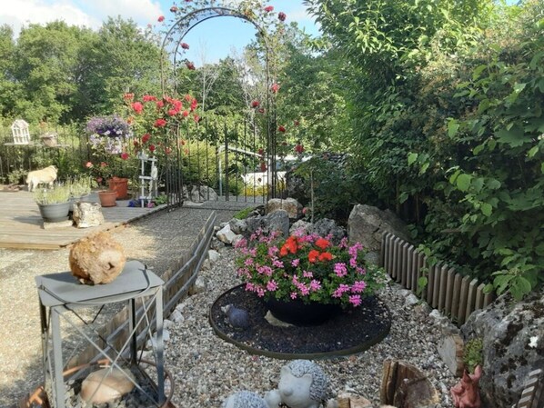 A garden with a metal table, a flower bed with pink flowers, and a metal archway. - Donautal Comfortable Holiday Residence (Irndorf)