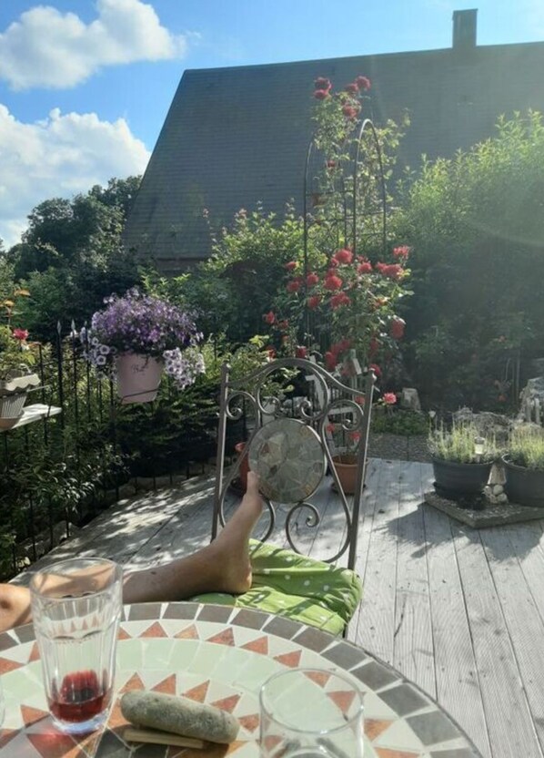 A wooden deck with a metal chair and a table with a glass of red drink and a stone. - Donautal Comfortable Holiday Residence (Irndorf)