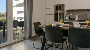 A modern kitchen with a dining area, featuring a large table with chairs, a built-in oven, and a coffee maker. - Villa Dora - Apt 3 "grijs" (Pula)