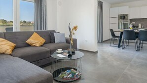 A modern living room with a grey sofa, a round coffee table, and a dining area with a kitchen in the background. - Villa Dora - Apt 3 "grijs" (Pula)
