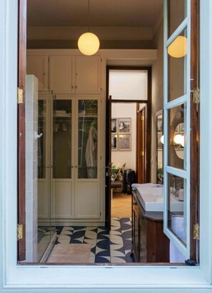 Een kamer met een grote garderobe, een bed, een nachtkastje en een raam met uitzicht op een andere kamer.