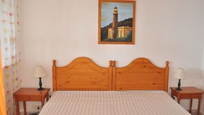 A bedroom with a wooden headboard, two bedside tables with lamps, a striped bedspread, and a painting of a lighthouse on the wall. - Casa Mar y Sol aan Zee (Los Llanos de Aridane)