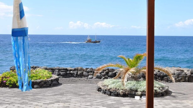 A covered outdoor area with a view of the ocean, a boat in the distance, and a decorative blue and white object. - Casa Mar y Sol aan Zee (Los Llanos de Aridane)