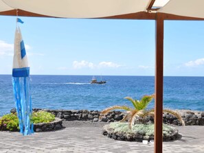 Un espacio al aire libre techado con vista al océano, un barco en la distancia y un objeto decorativo azul y blanco.