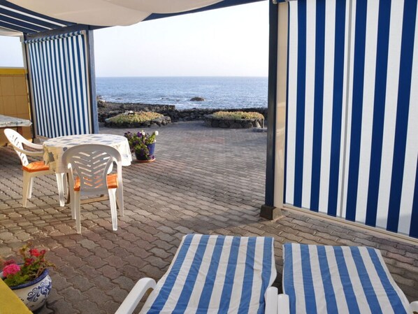 Un patio con mesa y sillas, un toldo a rayas y vista al mar.