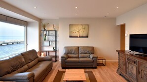 A modern living room with a leather sofa, a grey couch, a wooden coffee table, and a TV on a wooden cabinet. - Giannina 0001 Located at the Beach (De Haan)
