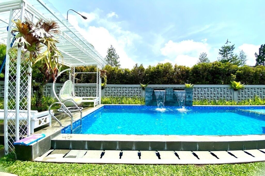 Una piscina con cascada, rodeada por una pérgola blanca y un muro de piedra.
