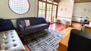 A living room with a sofa, a round window, and a dining area with a table and chairs. - SF Homey Yokohama (Cipanas)