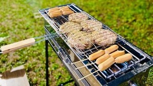 A portable grill with sausages and meat patties being cooked outdoors. - SF Homey Yokohama (Cipanas)