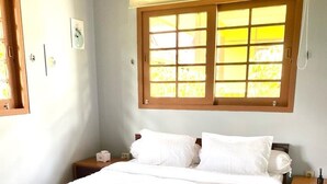A bedroom with a bed, two bedside tables, a window with blinds, and an air conditioning unit. - SF Homey Yokohama (Cipanas)