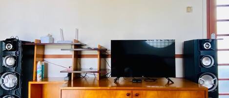A wooden entertainment center with a flat-screen TV, two large speakers, and a shelf with electronic devices.