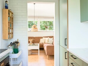 A modern kitchen with a wooden shelf, a dining area with a brown sofa, and a view of greenery outside. - 6 Person Holiday Home in Faaborg (Faaborg)
