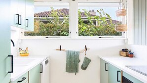 Cozinha com duas janelas, soalho de madeira e vista para uma casa com telhado de cerâmica.