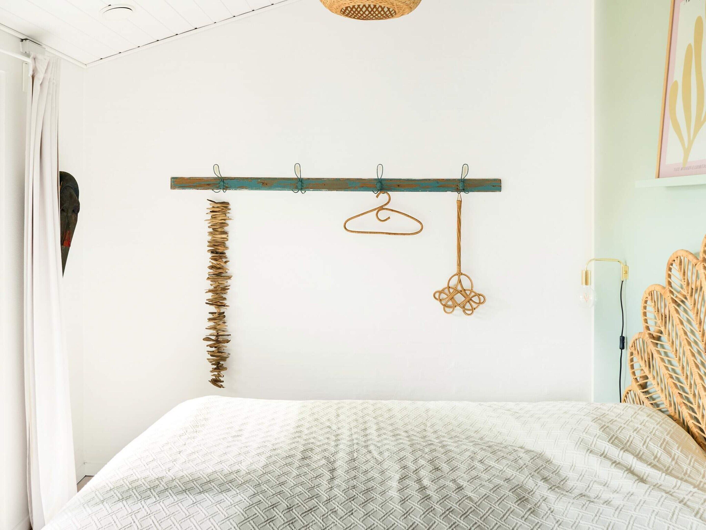 A bedroom with a bed, a wooden coat rack with a few items, and a wall-mounted light fixture.