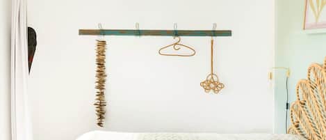 A bedroom with a bed, a wooden coat rack with a few items, and a wall-mounted light fixture.