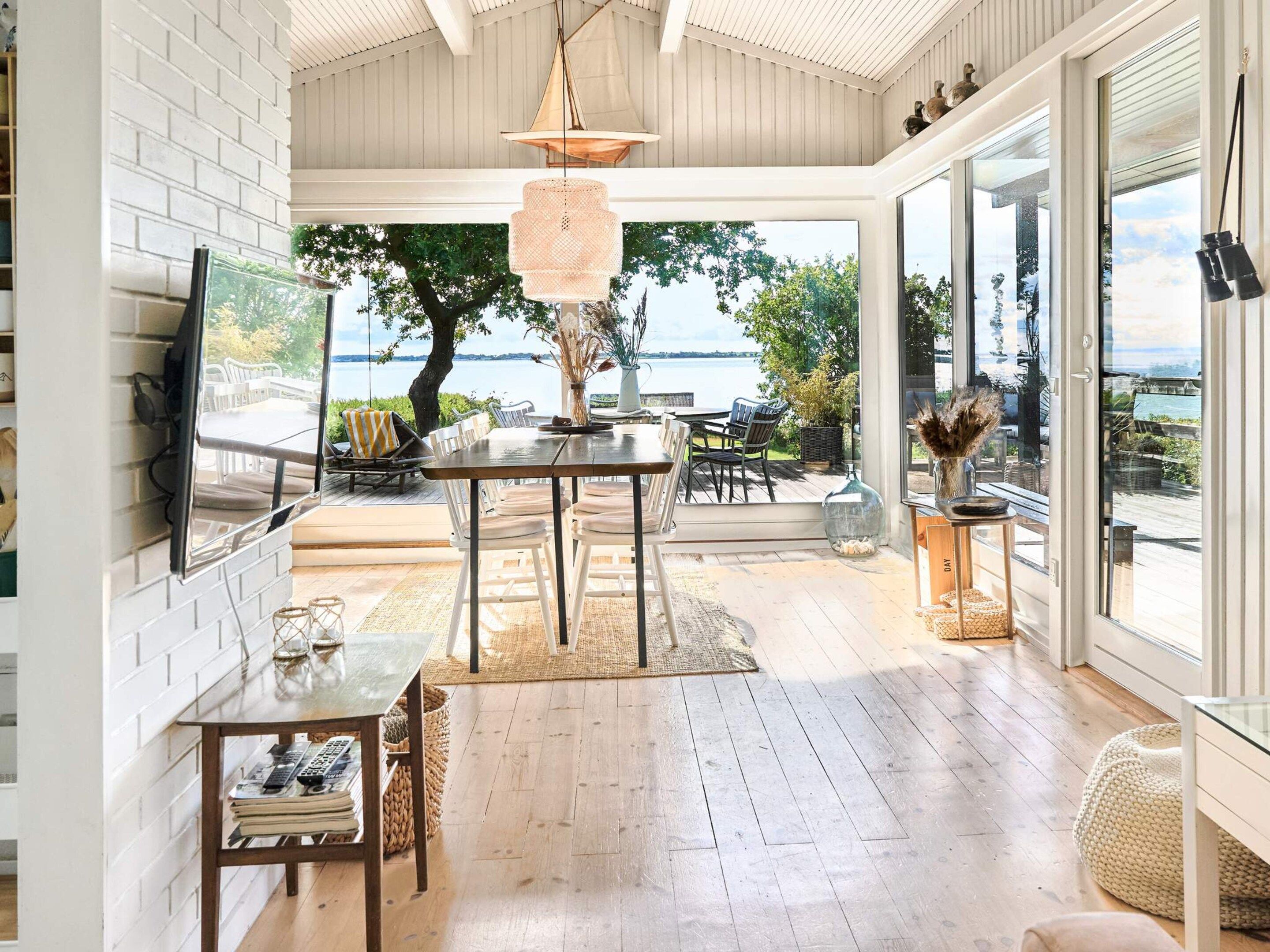 A spacious room with a wooden floor, a dining table, chairs, a television, and a view of the outdoors.